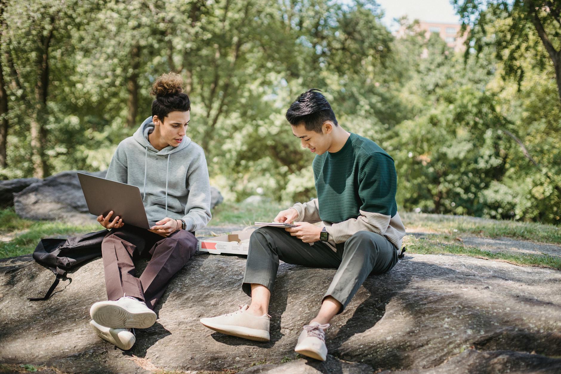 male friends sitting on boulder with laptop